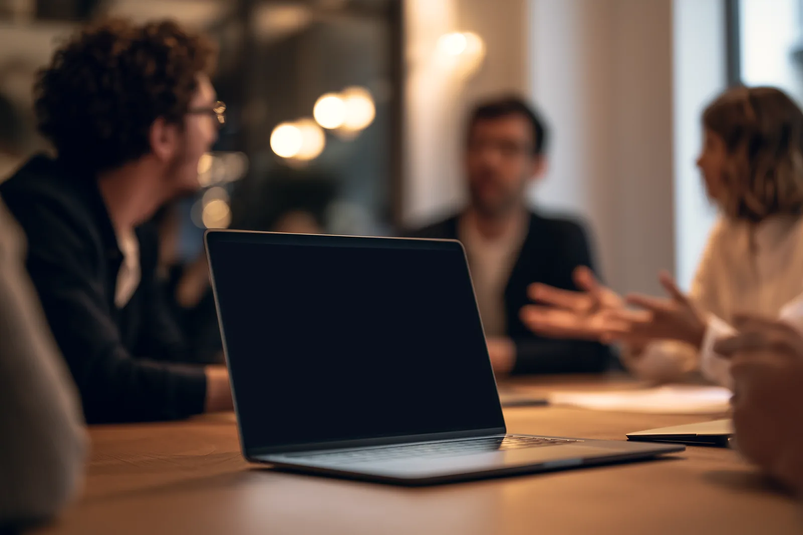 A meeting around a laptop; on its screen, a video call and Scribe’s small window recording it